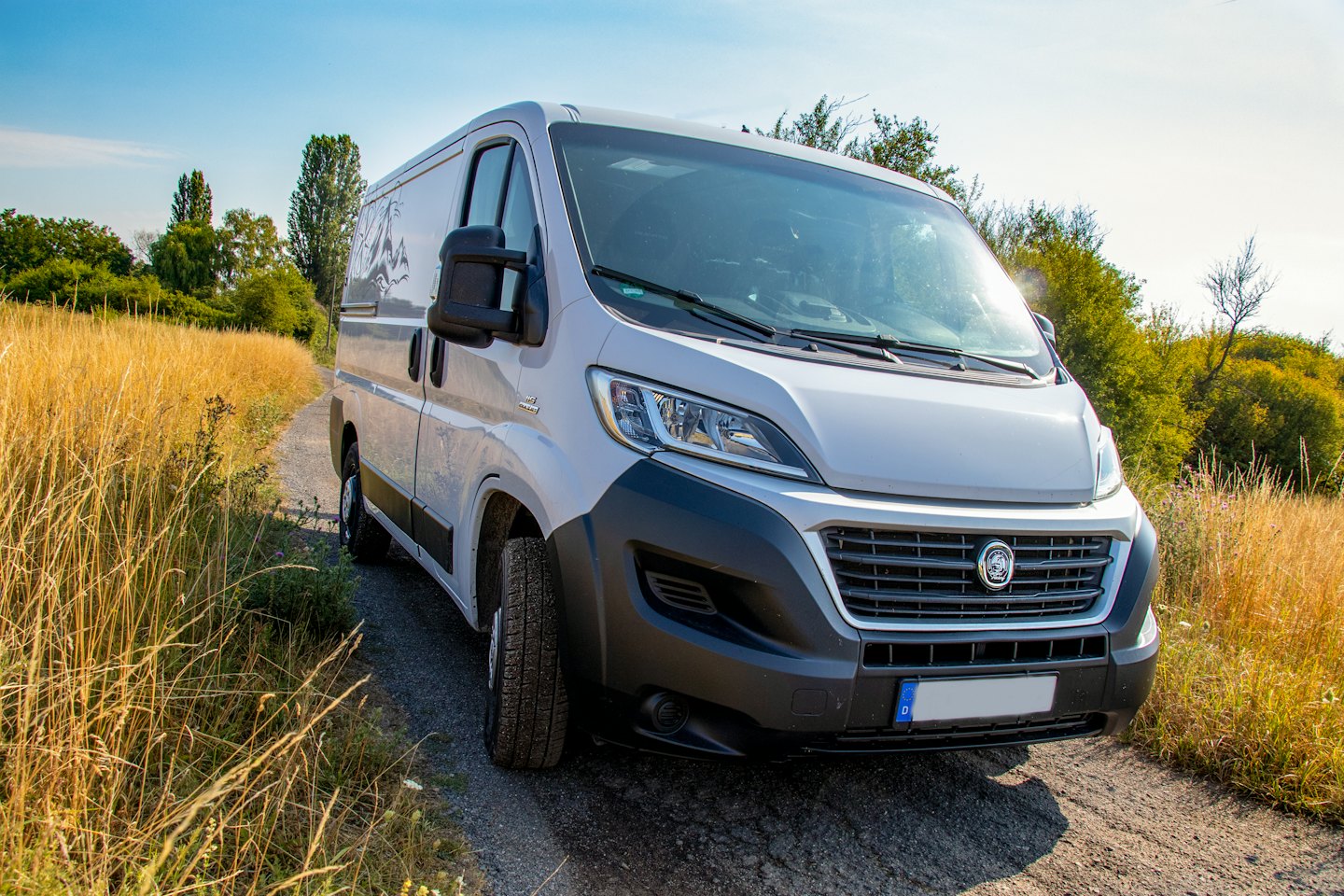 White panel van parked on a dirt path in grassy field.