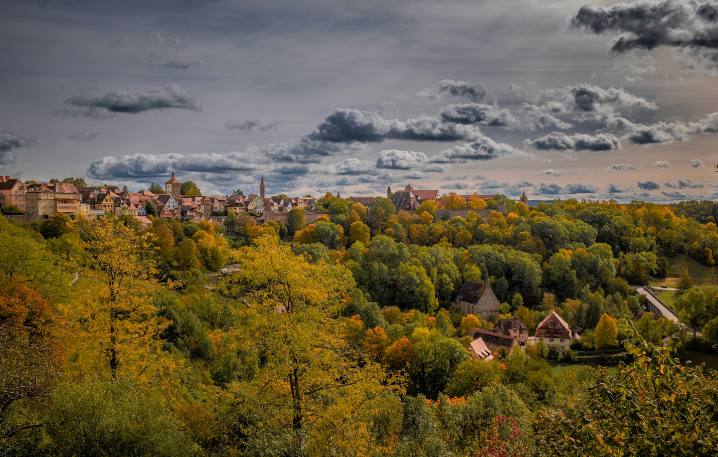 Medieval stone town buildings surrounded by dense autumn trees.