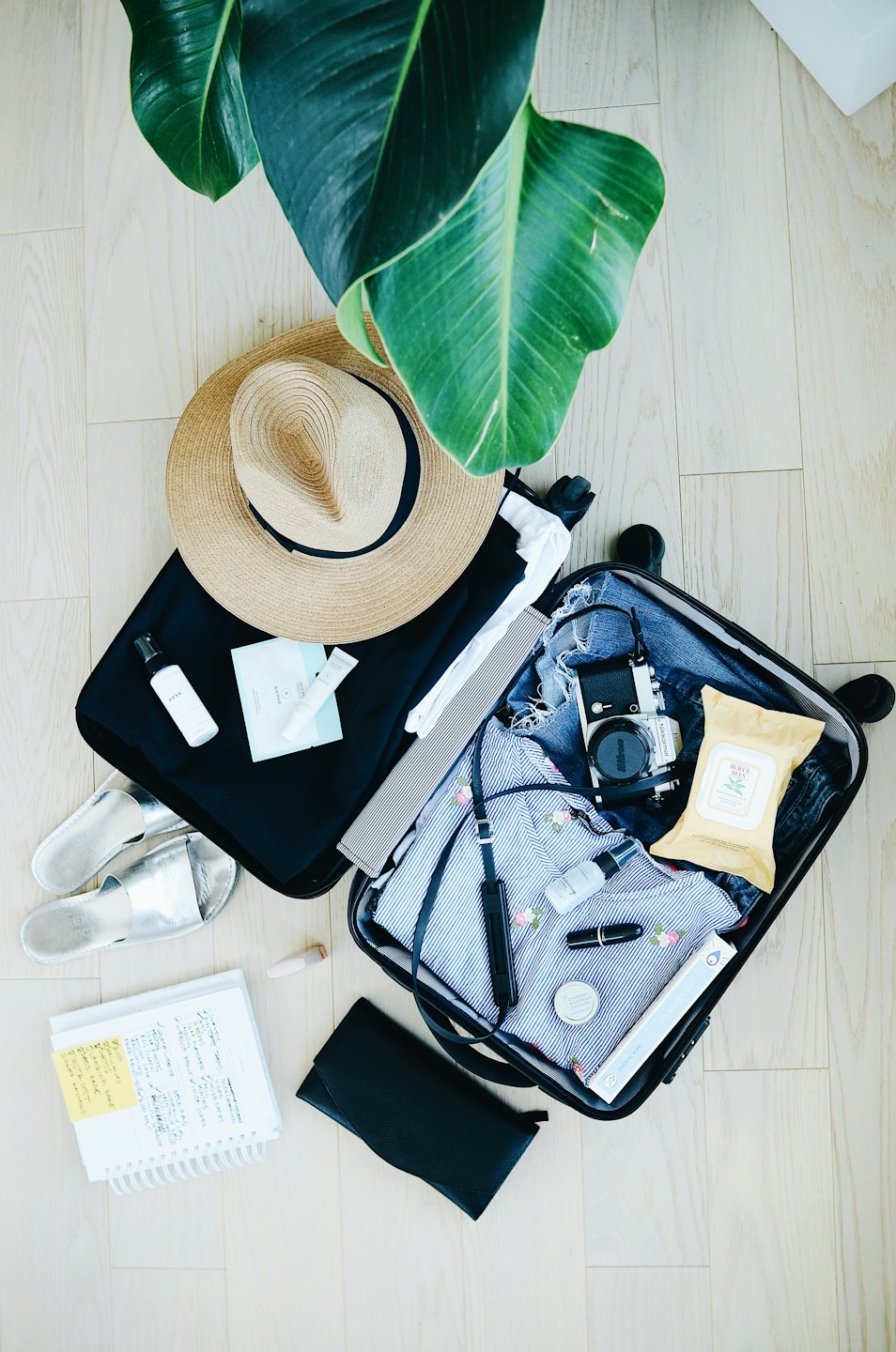 Black suitcase with travel essentials arranged on a wooden floor.